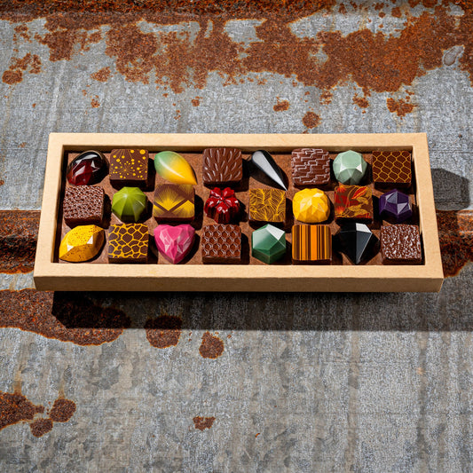 La feve's 24 assorted gemstone like colorful chocolates in a box on a textured metal surface