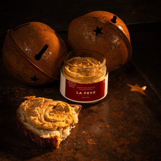 Jar of nutty spread on a dark surface with oranges and bread.