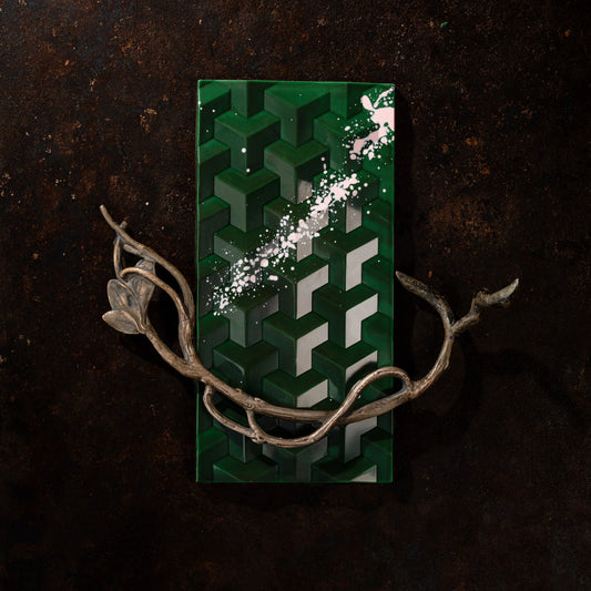 Green geometric patterned chocolate bar with white chocolate drizzle on a dark surface