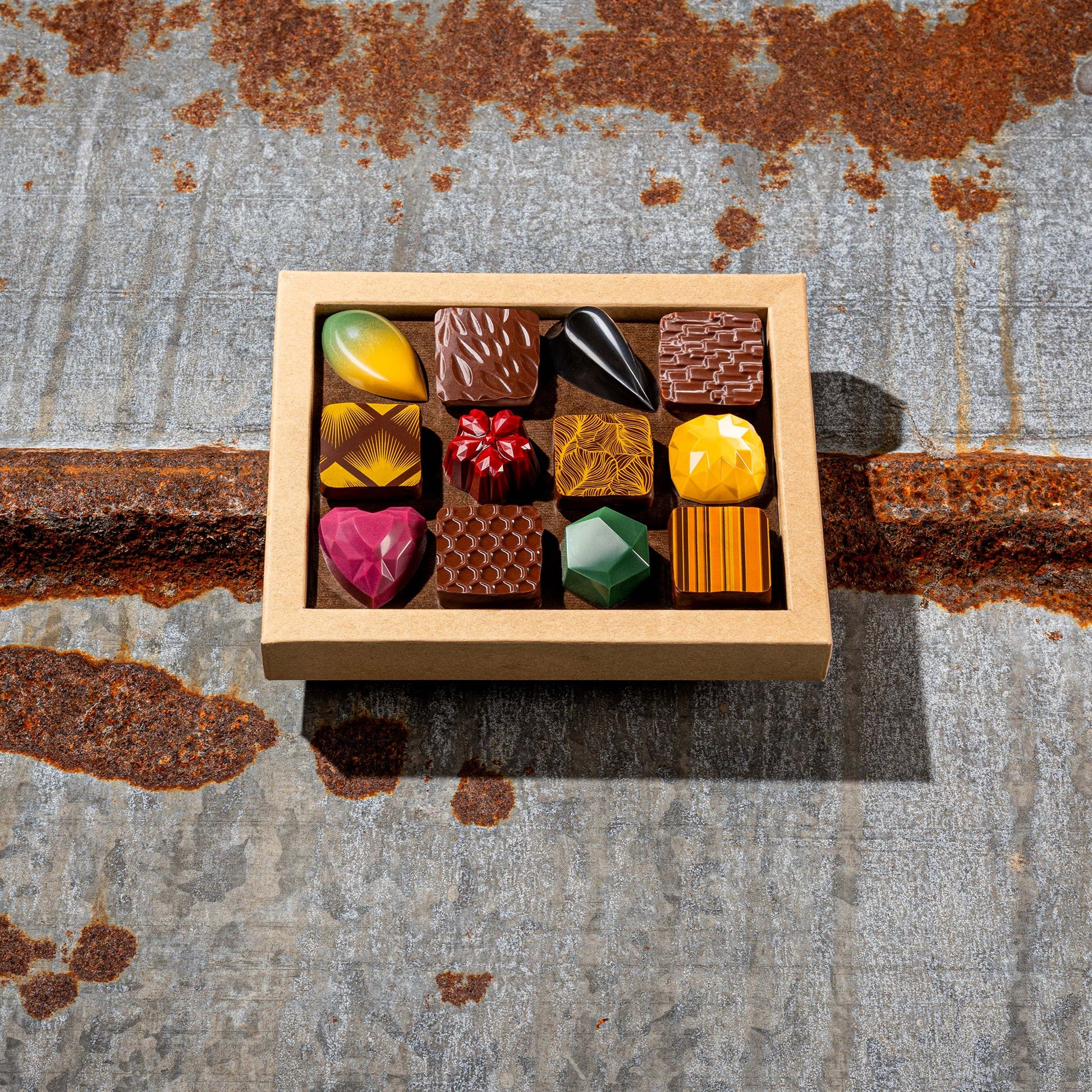 La Feve chocolate box of 12 colorful jewel-like chocolates on a textured metal surface