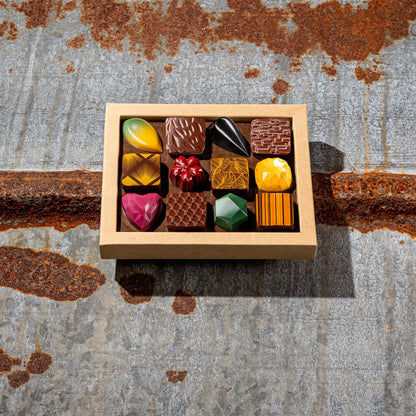 La Feve chocolate box of 12 colorful jewel-like chocolates on a textured metal surface