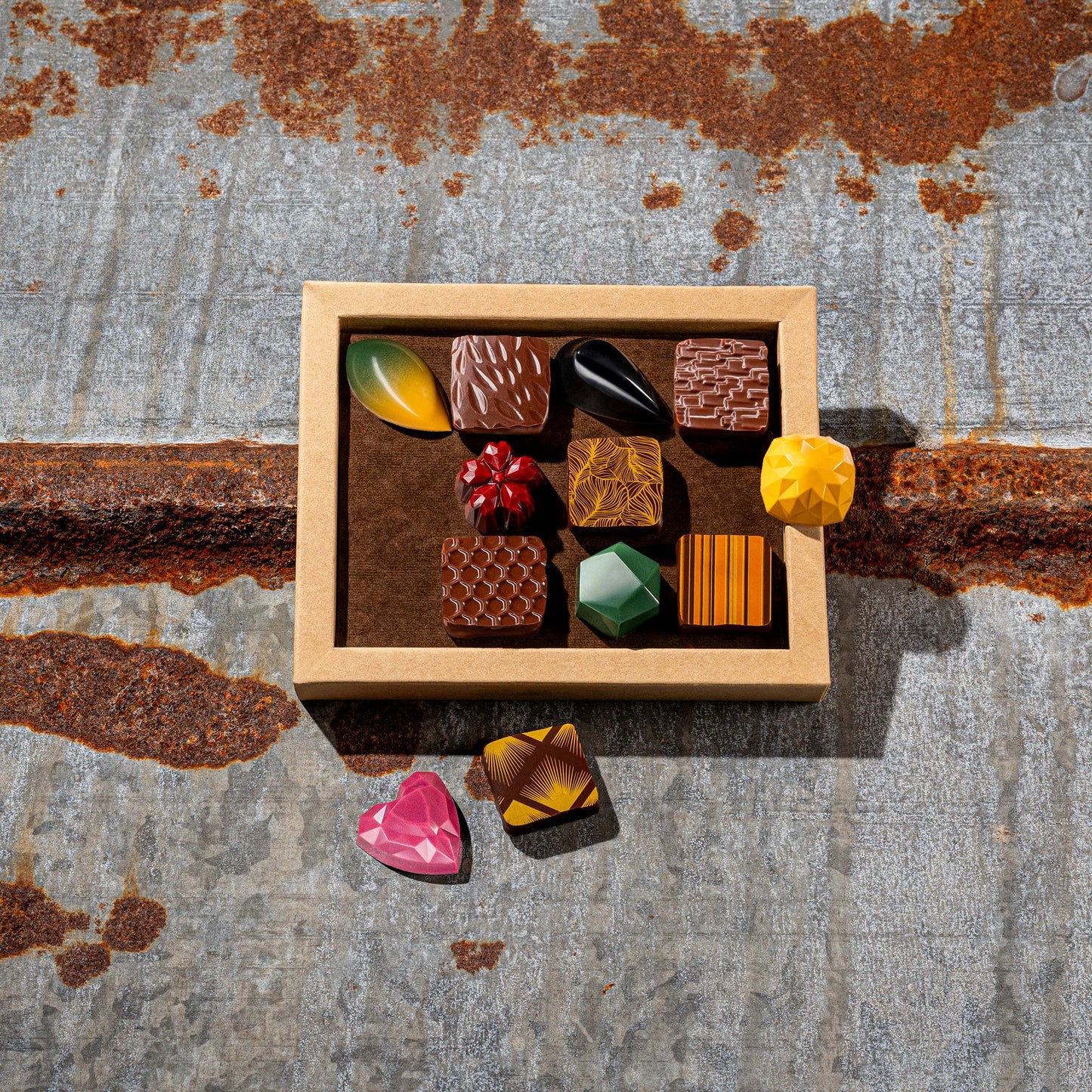 La Feve chocolate box of 12 colorful jewel-like chocolates on a textured metal surface