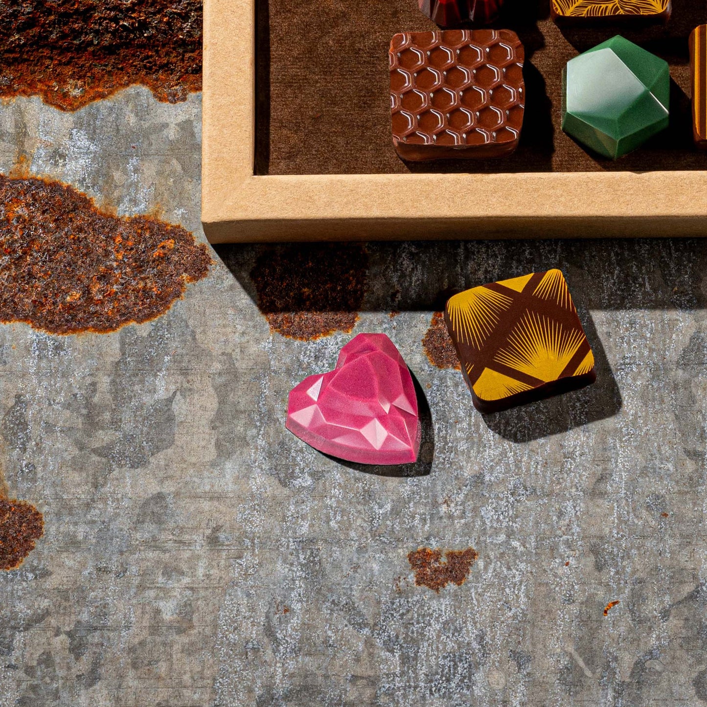 Colorful gemstone-like chocolates on a textured surface with a wooden box in the background.