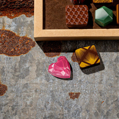 Colorful gemstone-like chocolates on a textured surface with a wooden box in the background.