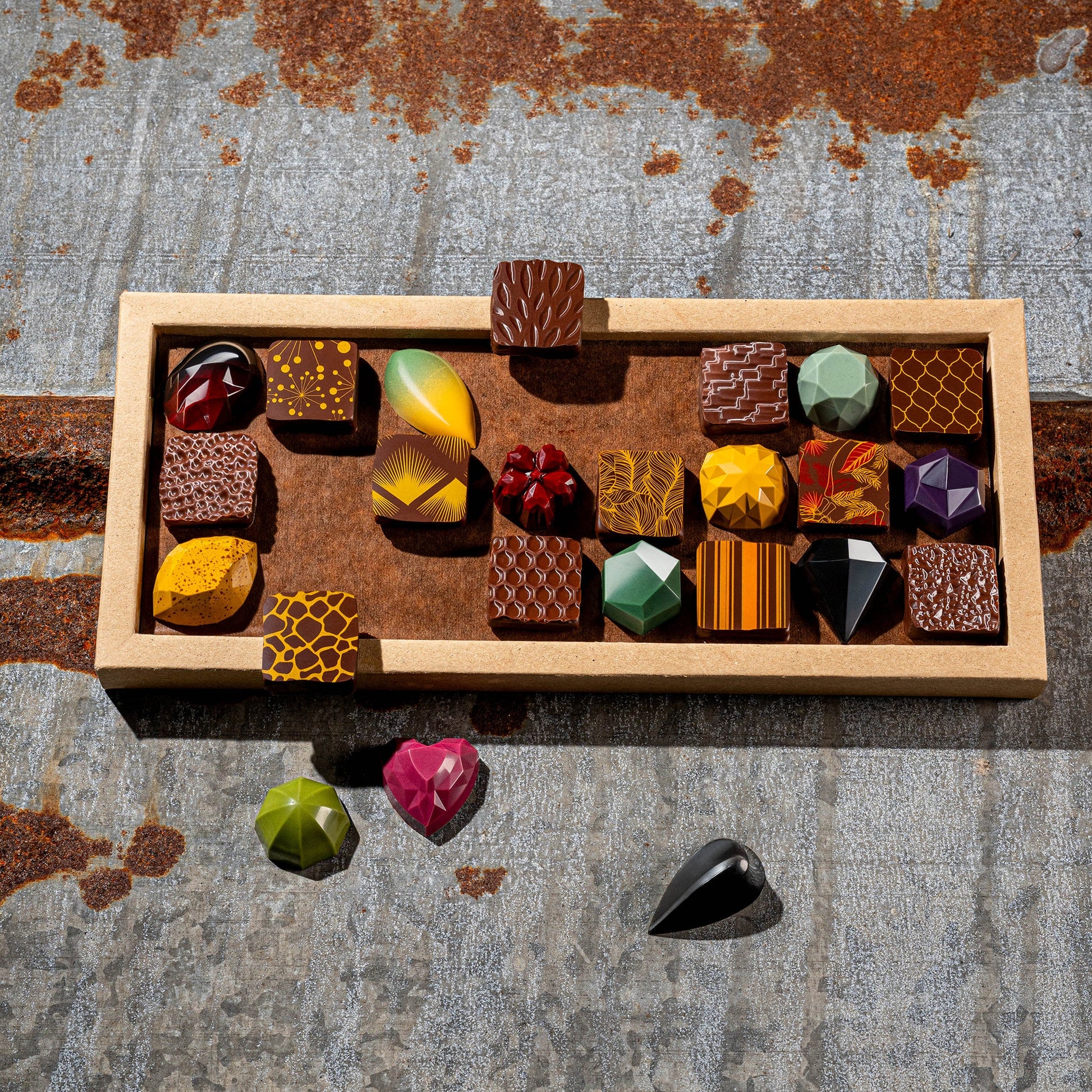 La feve's 24 assorted gemstone like colorful chocolates in a box on a textured metal surface