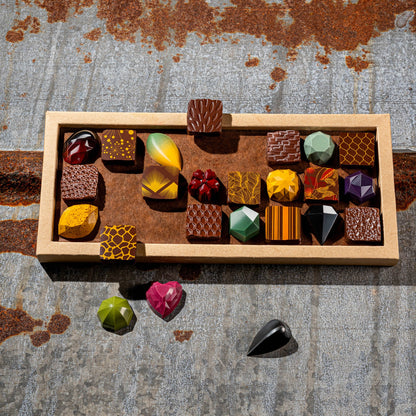 La feve's 24 assorted gemstone like colorful chocolates in a box on a textured metal surface