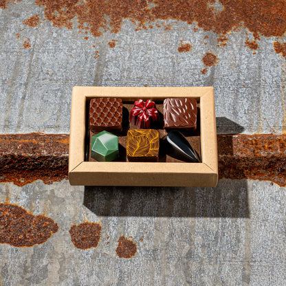La Feve chocolate box  with 6 flavours bonbons. 3 square pralines and 3 jewel shaped bonbons on a rustic metal surface