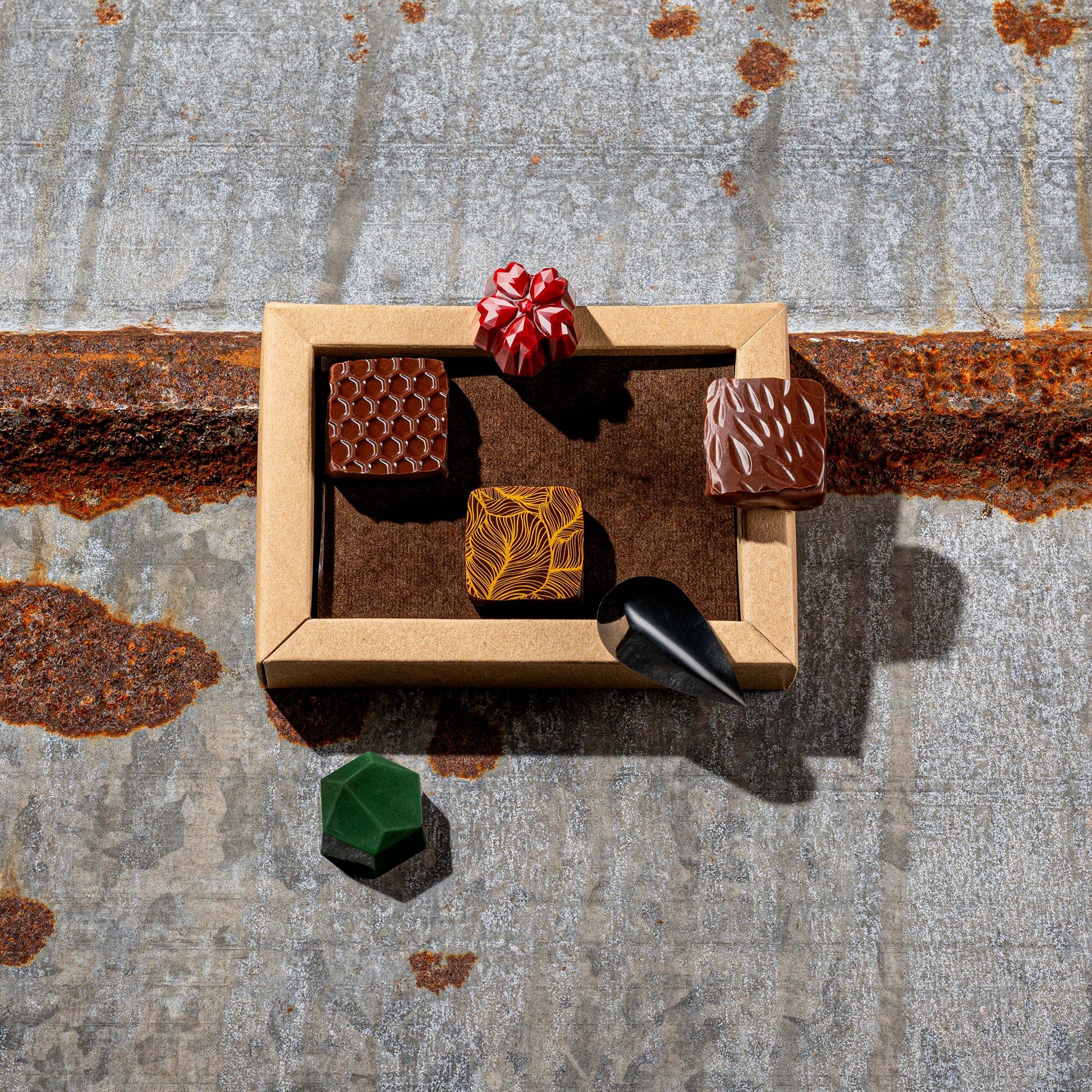 La Feve chocolate box  with 6 flavours bonbons. 3 square pralines and 3 jewel shaped bonbons on a rustic metal surface
