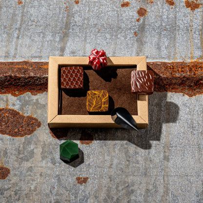La Feve chocolate box  with 6 flavours bonbons. 3 square pralines and 3 jewel shaped bonbons on a rustic metal surface