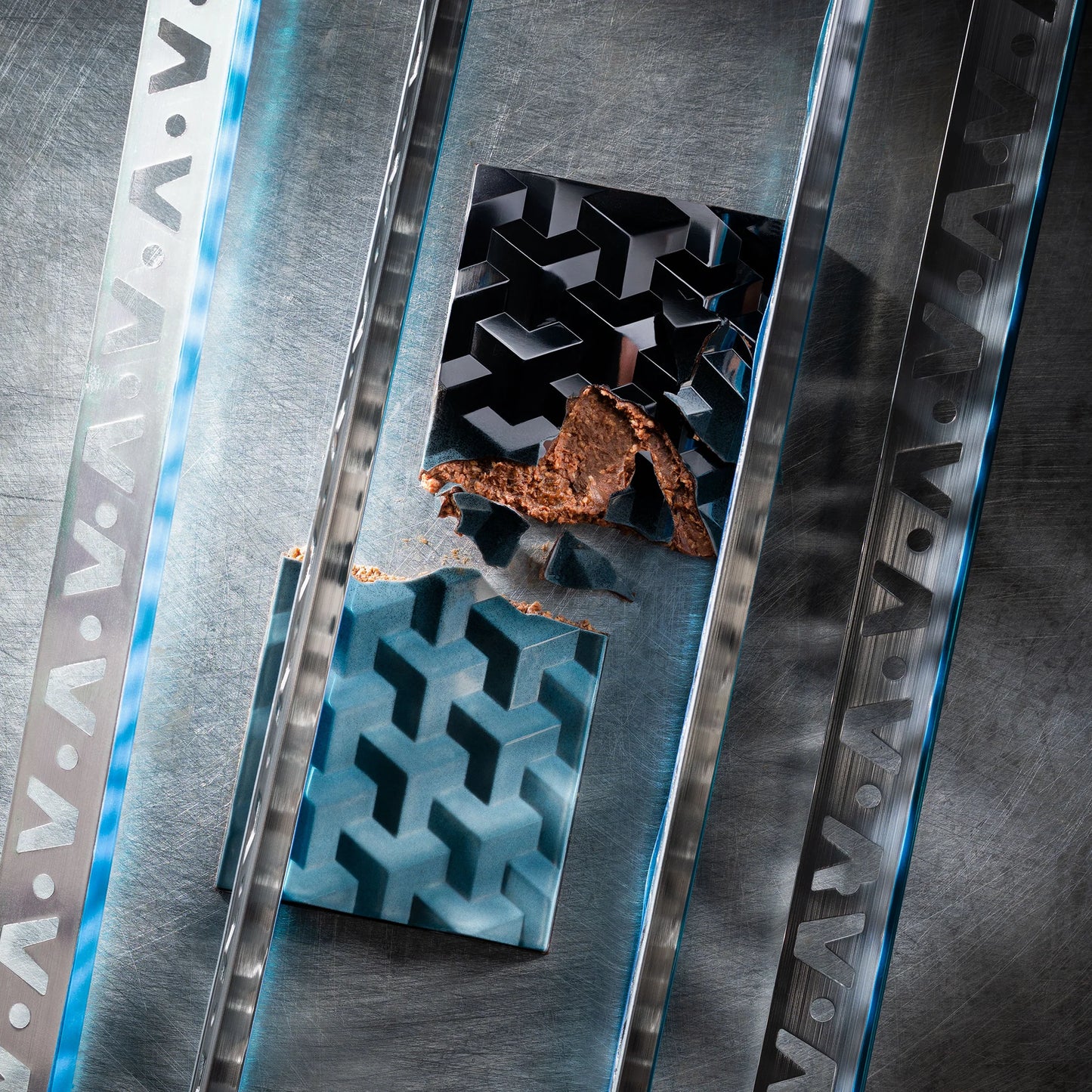 Teal chocolate bar with geometric design cut in half on a metal textured surface