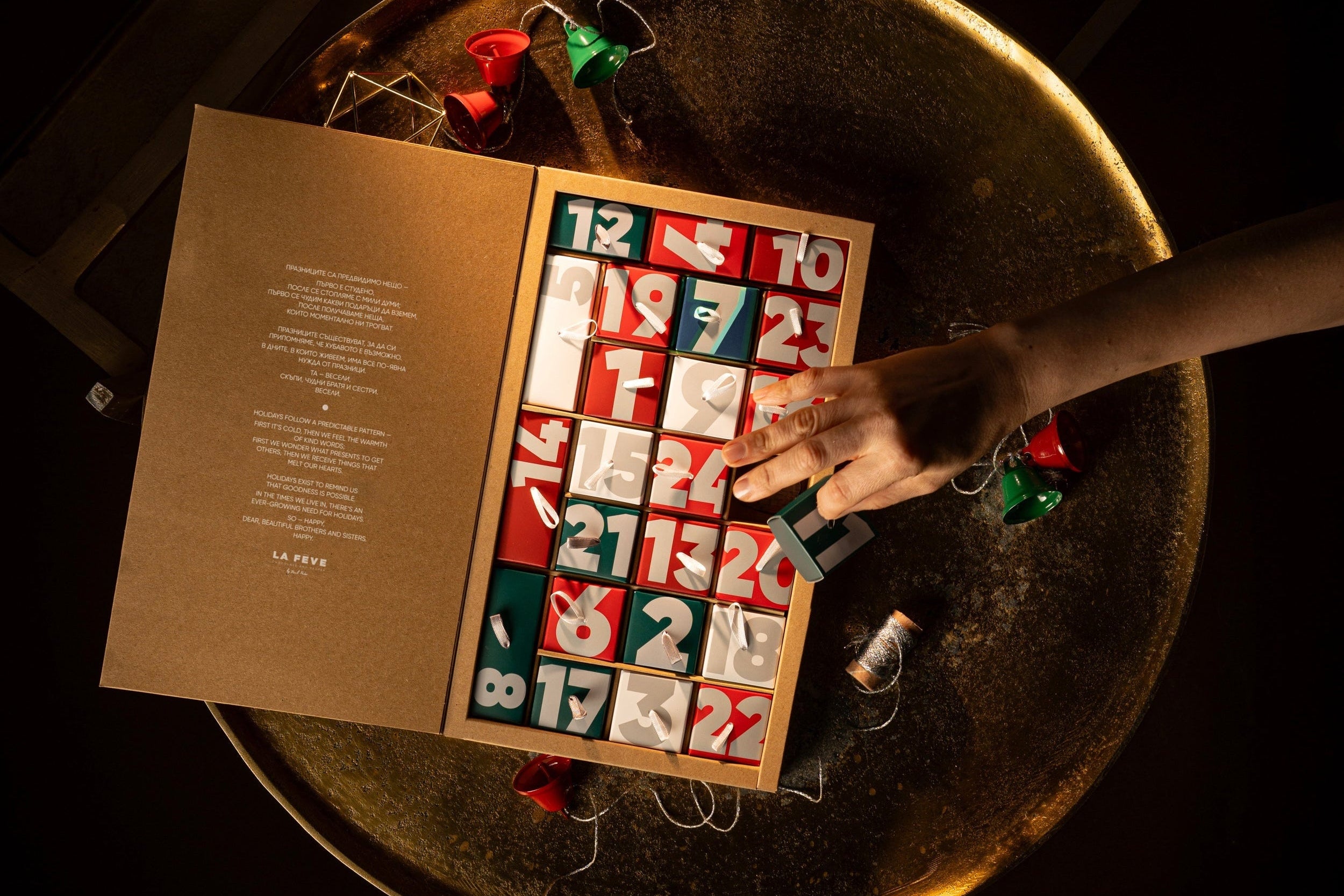 Person opening a Christmas advent calendar on a rustic table with string lights.