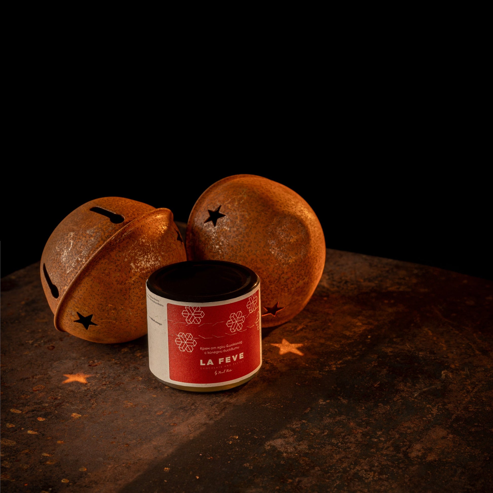 Decorative orange Christmas bells with black star patterns on a dark surface, featuring a red spread jar labeled 'La Féve'.