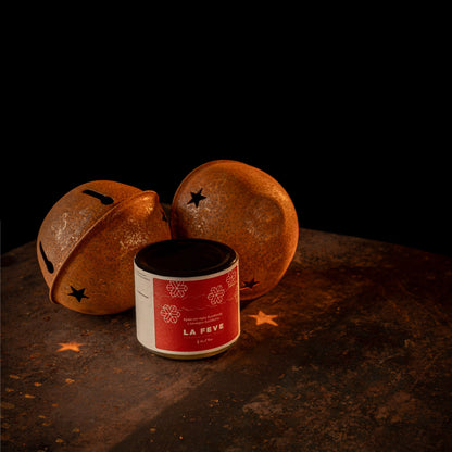 Decorative orange Christmas bells with black star patterns on a dark surface, featuring a red spread jar labeled 'La Féve'.